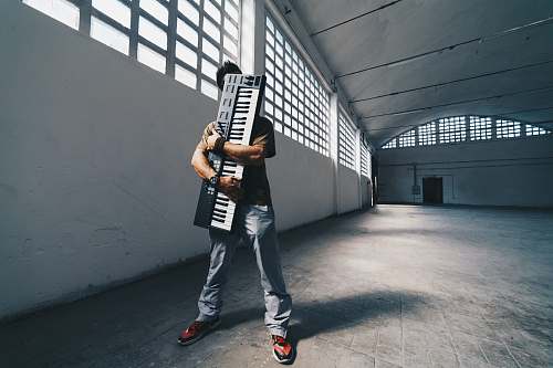 grey man hugging the electronic keyboard while standing inside room accordion